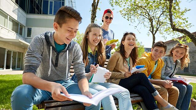Schüler:innen sitzen im Schulhof und lachen.