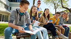 Schüler:innen sitzen im Schulhof und lachen.