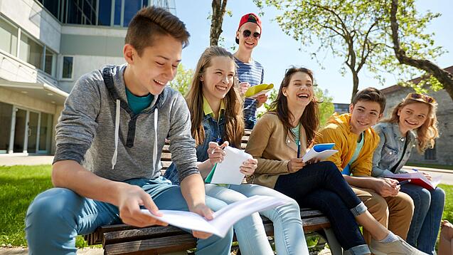 Schüler:innen sitzen im Schulhof und lachen.