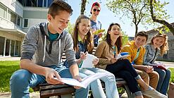 Schüler:innen sitzen im Schulhof und lachen.