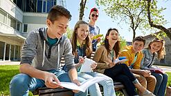 Schüler:innen sitzen im Schulhof und lachen.