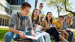 Schüler:innen sitzen im Schulhof und lachen.