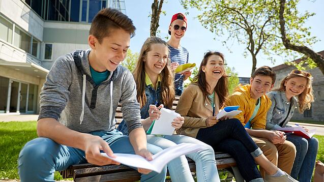 Schüler:innen sitzen im Schulhof und lachen.