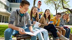 Schüler:innen sitzen im Schulhof und lachen.