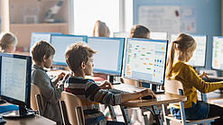 Schülerinnen und Schüler sitzen vor Computern in einem Klassenzimmer.