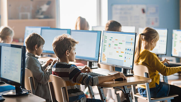 Schülerinnen und Schüler sitzen vor Computern in einem Klassenzimmer.