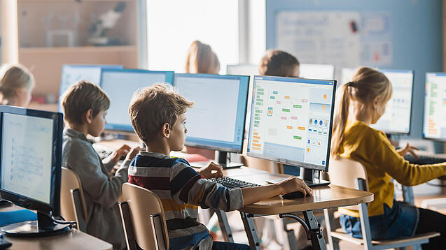 Schülerinnen und Schüler sitzen vor Computern in einem Klassenzimmer.