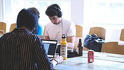 Oberstufenschüler oder junge Studierende sitzen an einem Tisch und arbeiten an Laptops.