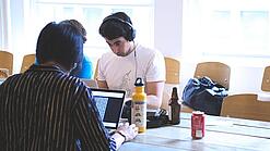 Oberstufenschüler oder junge Studierende sitzen an einem Tisch und arbeiten an Laptops.