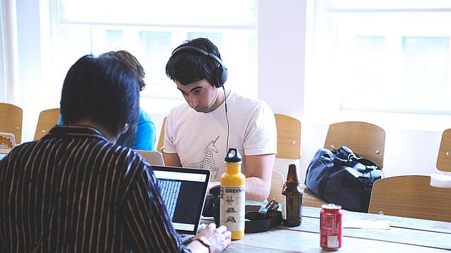 Oberstufenschüler oder junge Studierende sitzen an einem Tisch und arbeiten an Laptops.