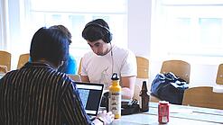 Oberstufenschüler oder junge Studierende sitzen an einem Tisch und arbeiten an Laptops.