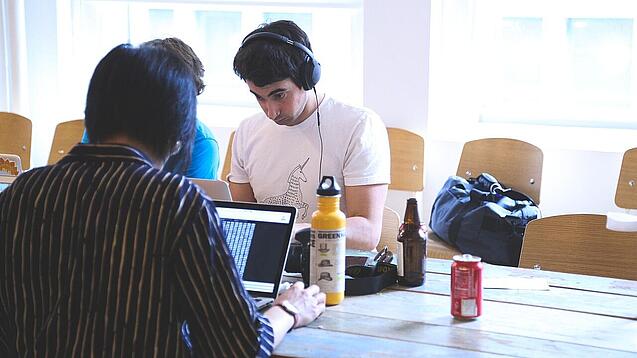 Oberstufenschüler oder junge Studierende sitzen an einem Tisch und arbeiten an Laptops.