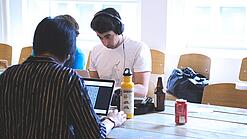 Oberstufenschüler oder junge Studierende sitzen an einem Tisch und arbeiten an Laptops.