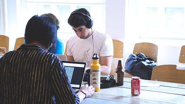 Oberstufenschüler oder junge Studierende sitzen an einem Tisch und arbeiten an Laptops.