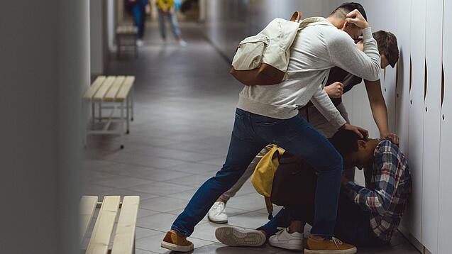 Zwei Schüler prügeln auf einen am Boden sitzenden Schüler ein.
