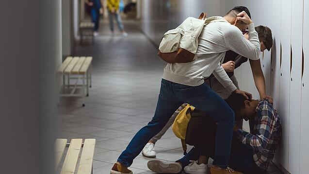 Zwei Schüler prügeln auf einen am Boden sitzenden Schüler ein.
