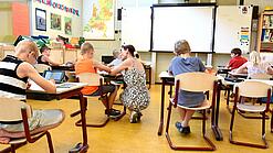 Kinder sitzen an Tischen in einem Klassenzimmer.