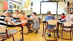 Kinder sitzen an Tischen in einem Klassenzimmer.