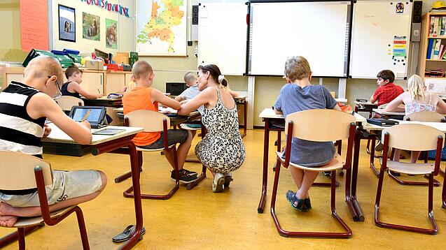 Kinder sitzen an Tischen in einem Klassenzimmer.