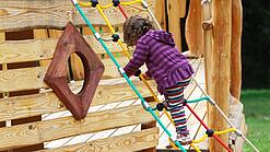 Ein Kind klettert auf einem Spielplatz an einem Spielgerät.