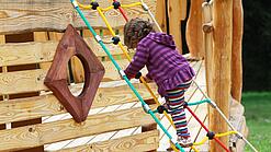 Ein Kind klettert auf einem Spielplatz an einem Spielgerät.