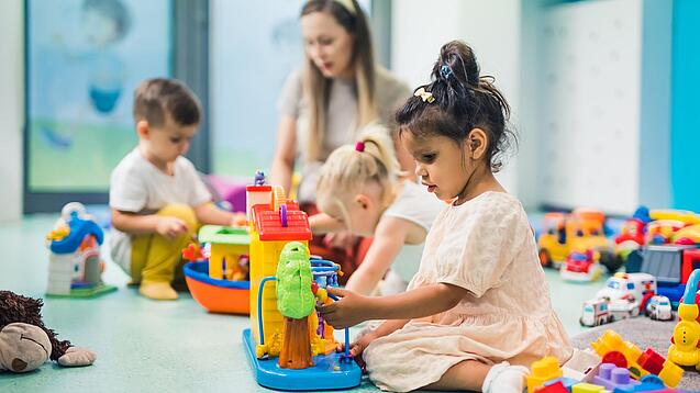 Kinder sitzen mit einer Erzieherin auf dem Boden und spielen.
