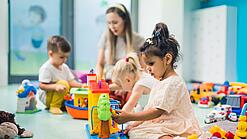 Kinder sitzen mit einer Erzieherin auf dem Boden und spielen.