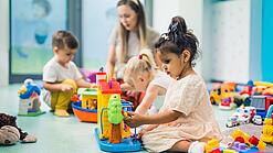 Kinder sitzen mit einer Erzieherin auf dem Boden und spielen.