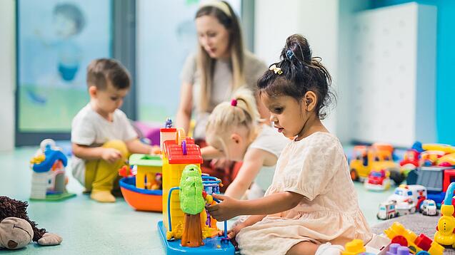Kinder sitzen mit einer Erzieherin auf dem Boden und spielen.