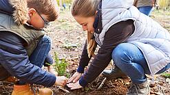 Zwei Jugendliche hocken auf dem Boden und pflanzen einen Baum ein.