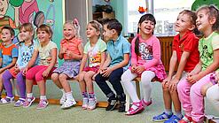 Kinder sitzen auf einer Bank in einer Kita.