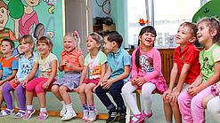 Kinder sitzen auf einer Bank in einer Kita.