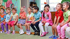 Kinder sitzen auf einer Bank in einer Kita.