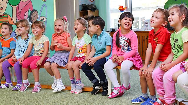Kinder sitzen auf einer Bank in einer Kita.