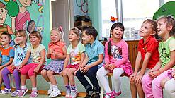 Kinder sitzen auf einer Bank in einer Kita.