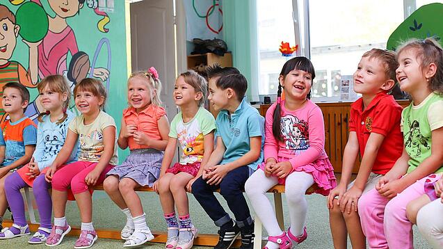 Kinder sitzen auf einer Bank in einer Kita.