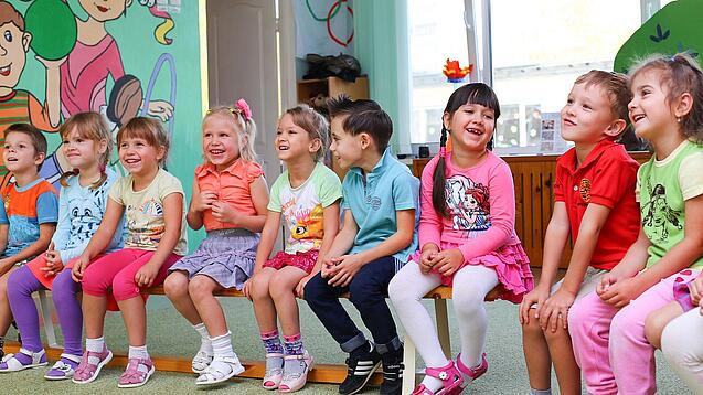 Kinder sitzen auf einer Bank in einer Kita.