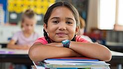 Ein Mädchen lehnt sich mit den Armen auf einen Stapel Schulhefte.