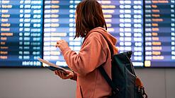 Junge Frau steht vor einer Anzeigetafel an einem Flughafen.