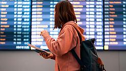 Junge Frau steht vor einer Anzeigetafel an einem Flughafen.