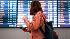 Junge Frau steht vor einer Anzeigetafel an einem Flughafen.