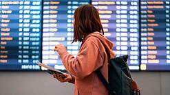 Junge Frau steht vor einer Anzeigetafel an einem Flughafen.