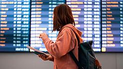 Junge Frau steht vor einer Anzeigetafel an einem Flughafen.