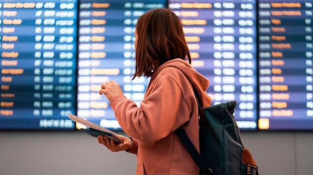 Junge Frau steht vor einer Anzeigetafel an einem Flughafen.