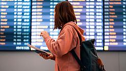 Junge Frau steht vor einer Anzeigetafel an einem Flughafen.