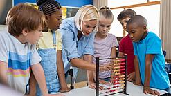Eine Lehrerin erklärt einer Gruppe von Grundschulkindern etwas an einem Rechenschieber.