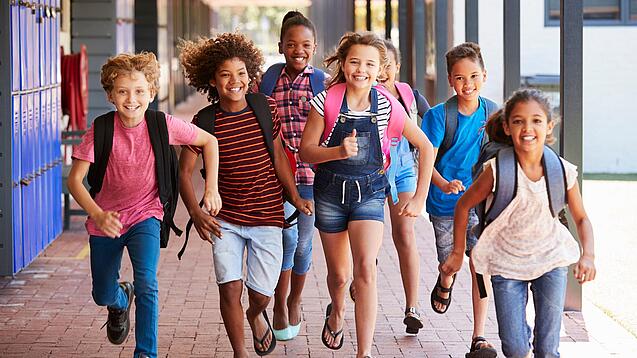 Eine Gruppe Kinder rennt auf dem Pausenhof in Richtung der Kamera.
