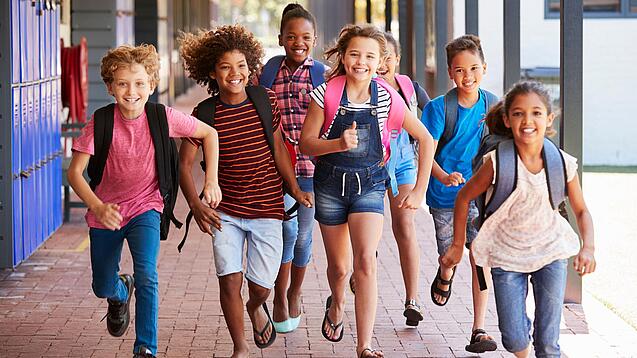Eine Gruppe Kinder rennt auf dem Pausenhof in Richtung der Kamera.