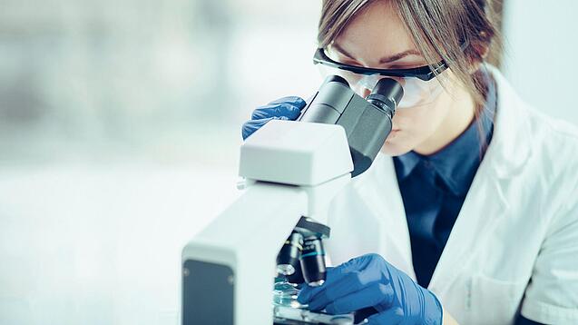 Eine Wissenschaftlerin schaut in ein Mikroskop.