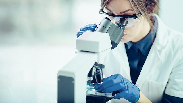Eine Wissenschaftlerin schaut in ein Mikroskop.